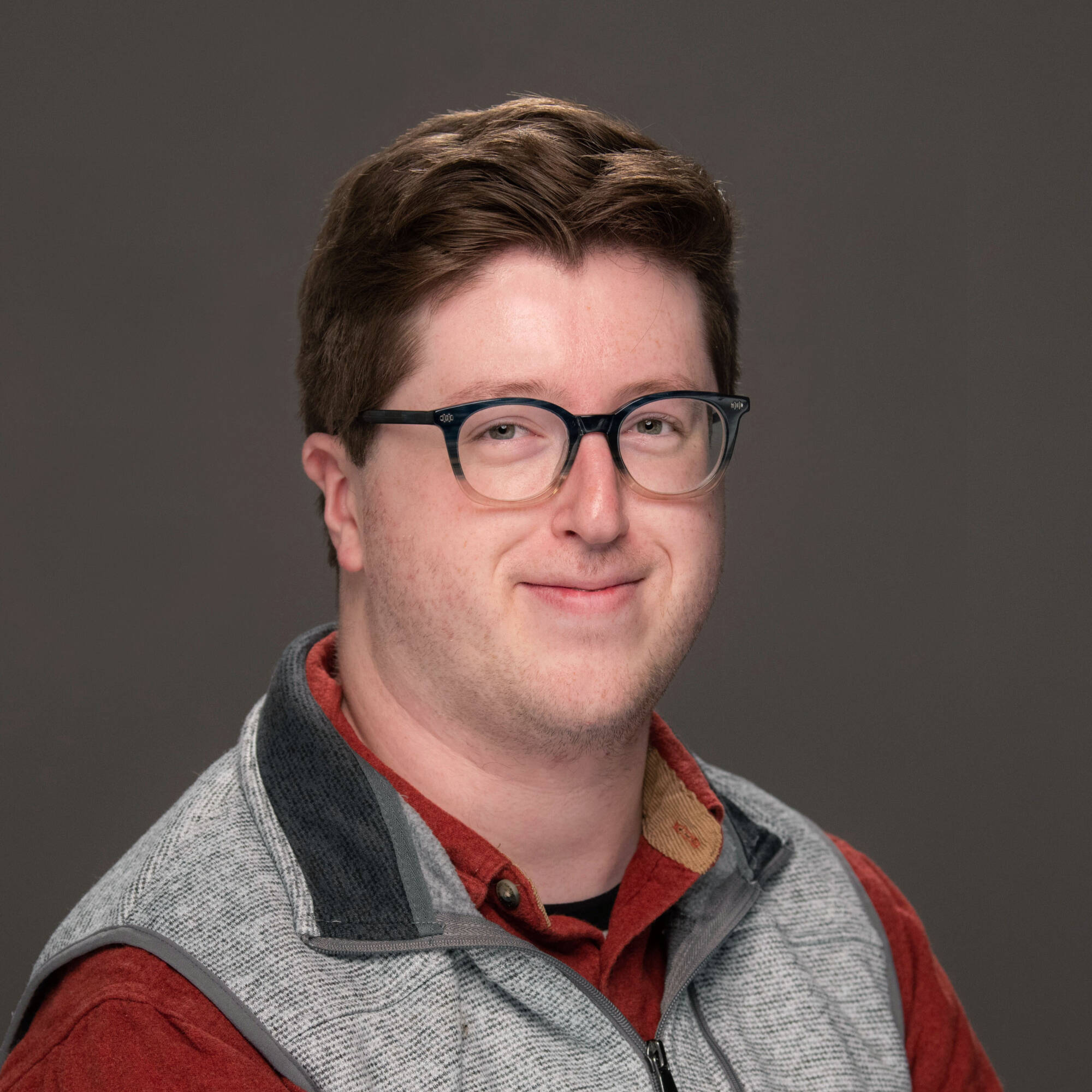 Jackson VanHaitsma in an orange shirt with a grey vest, looking cheerfully at the camera.